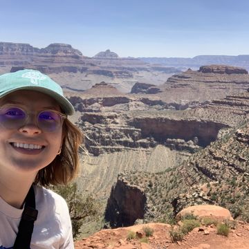 Against a backdrop of the South Rim of the Grand Canyon, Carly Taylor smiles at the camera wearing a blue baseball cap