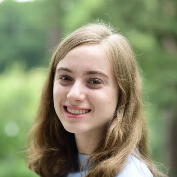 A headshot of student Lilly Salus, smiling at the camera with blonde, shoulder length hair against a green background.