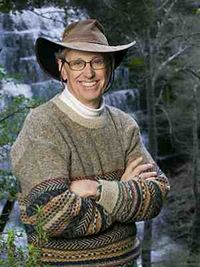 Photo of Professor David Freyberg outside in a sweater and brown brimmed hat with a waterfall behind him.