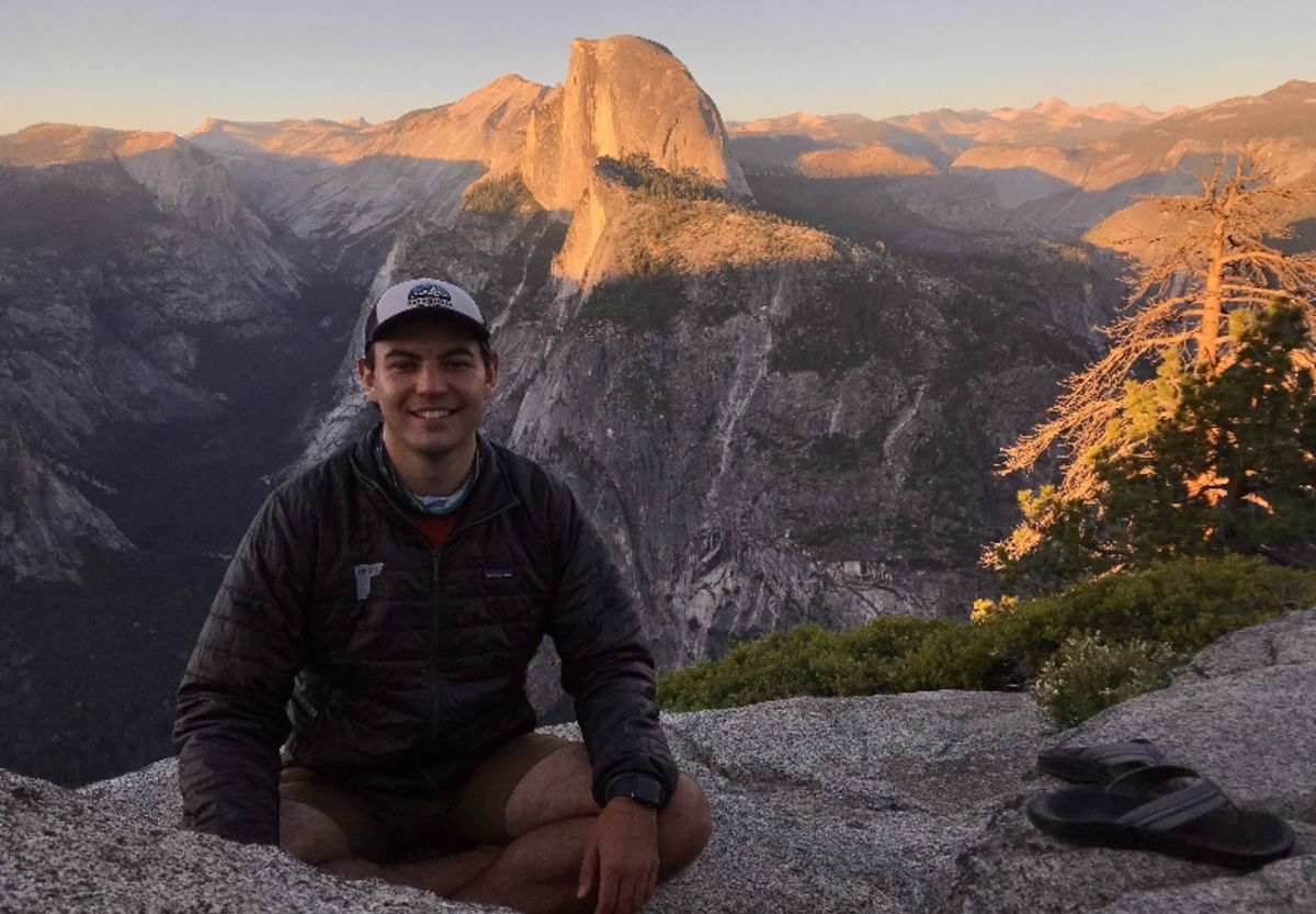 Nick Mascarello sits outside on a mountain plateau with mountains in the background