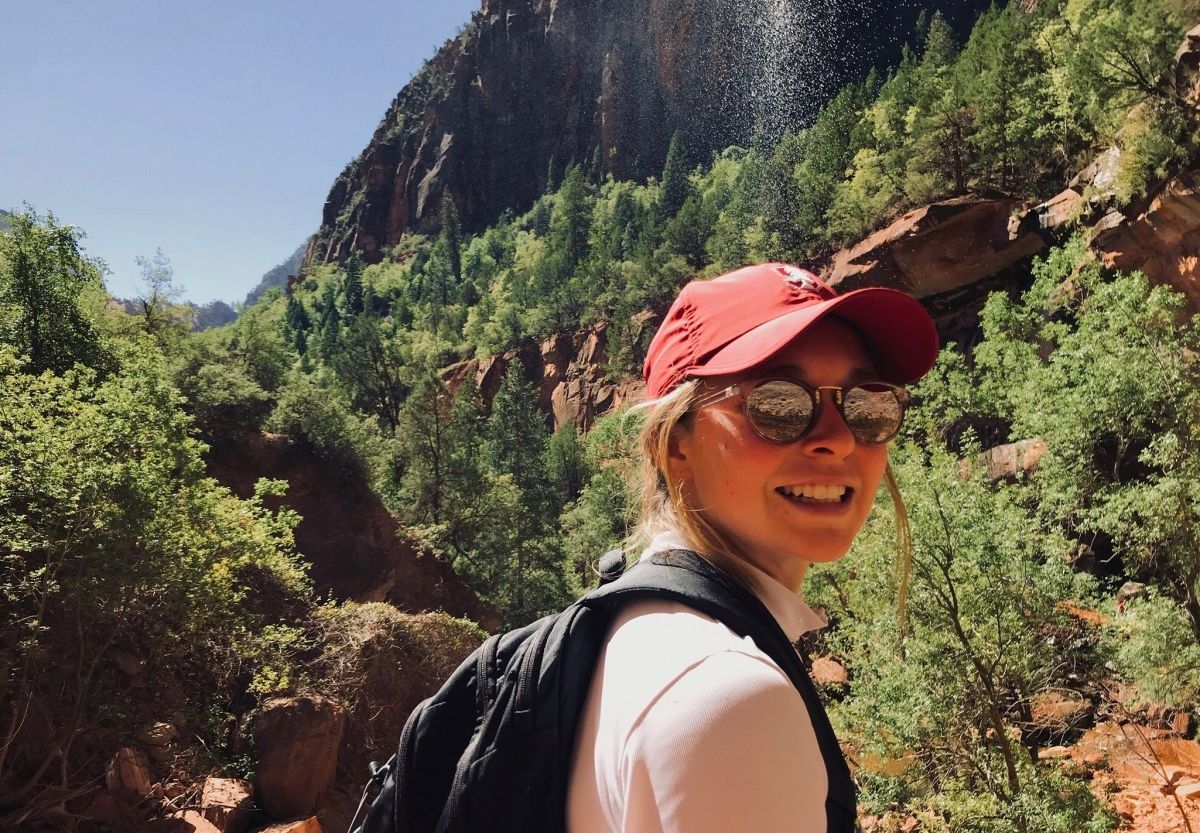 Sophia Boyd-Fliegel in a red baseball cap and sunglasses with mountains in the background
