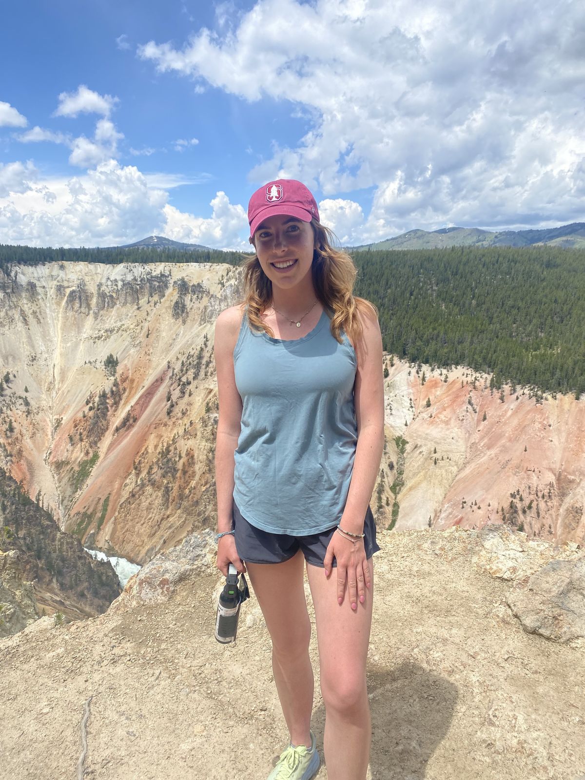 Elisabeth Westerman stands in a tank top, shorts and a red cap with the Grand Canyon and blue sky in the background.